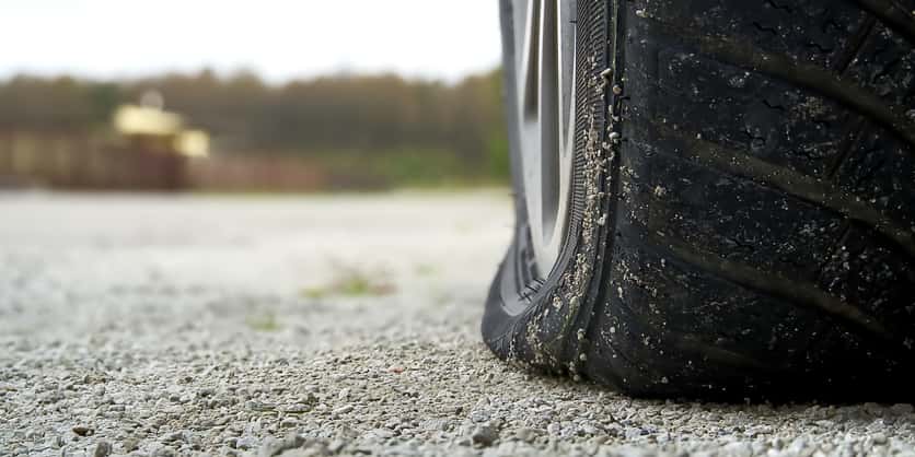 A flat tire parked on a gravel road. 