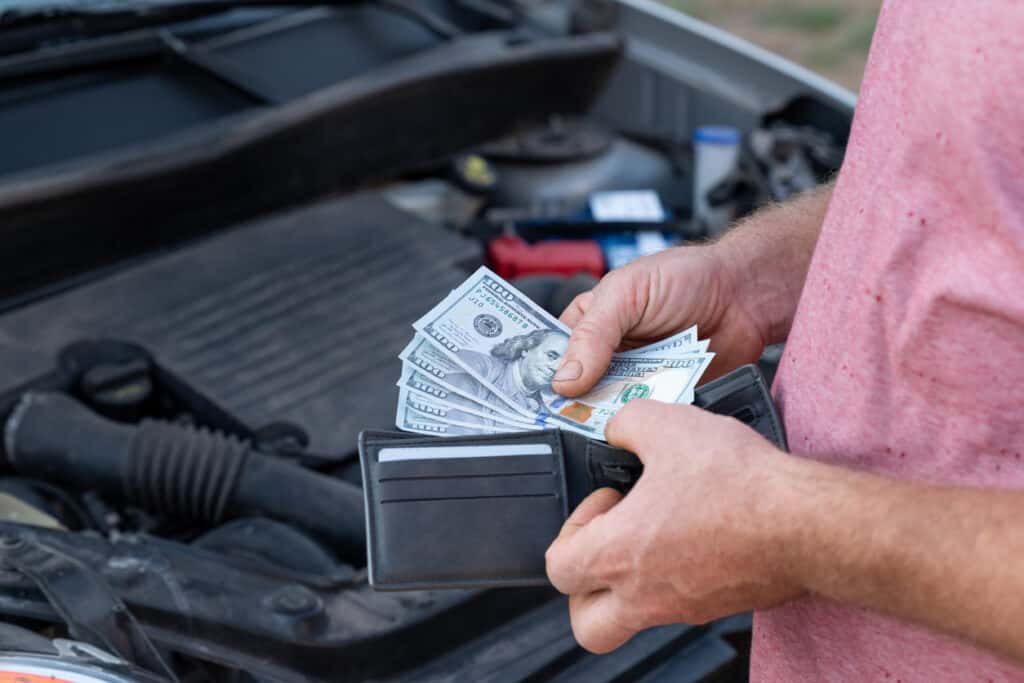 A man pull several hundred dollar bills out to pay for his broken engine repair.
