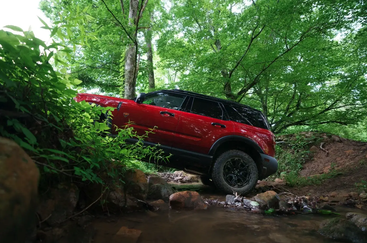 Red 2025 Ford Bronco Sport Off-Roading in a forest across a stream