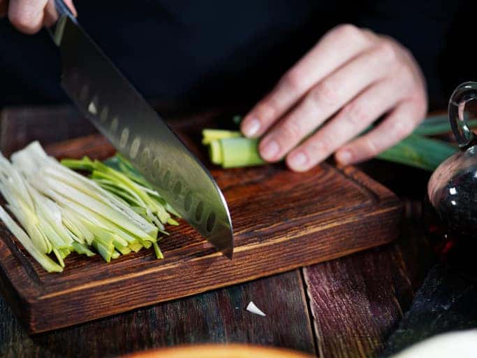 Person chopping leeks are wooden cutting board