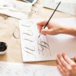 calligraphy, handwriting, technique concept. woman with beautiful elegant hands inscribing capital russian letters carefully in italic type with black ink and thin brush, drawing