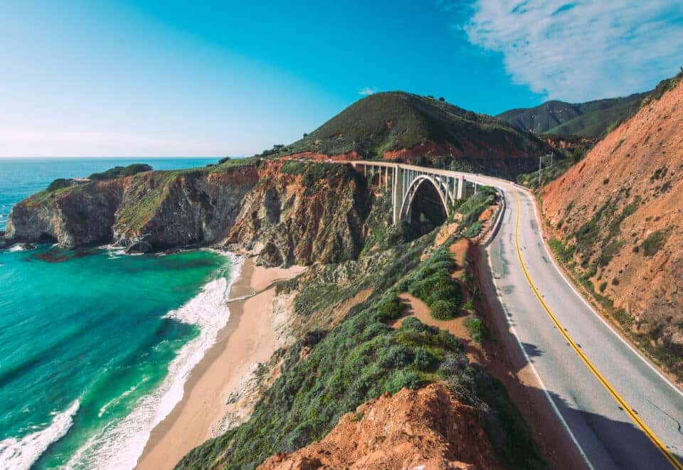 Winding sea-side road with a tall hill on one side.