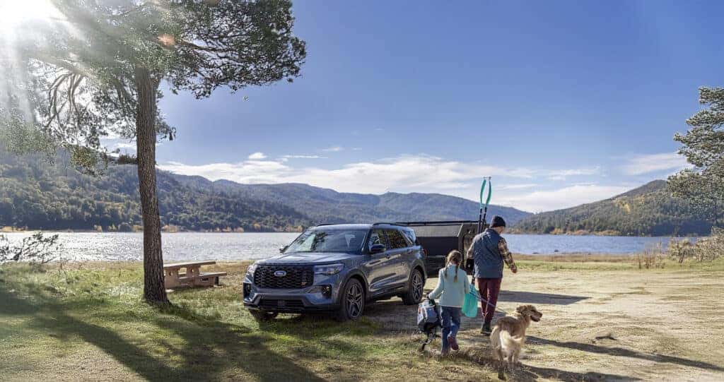 2025 Ford Explorer vapor blue parked by a lake with a family walking to the water with a dog and kayak paddles