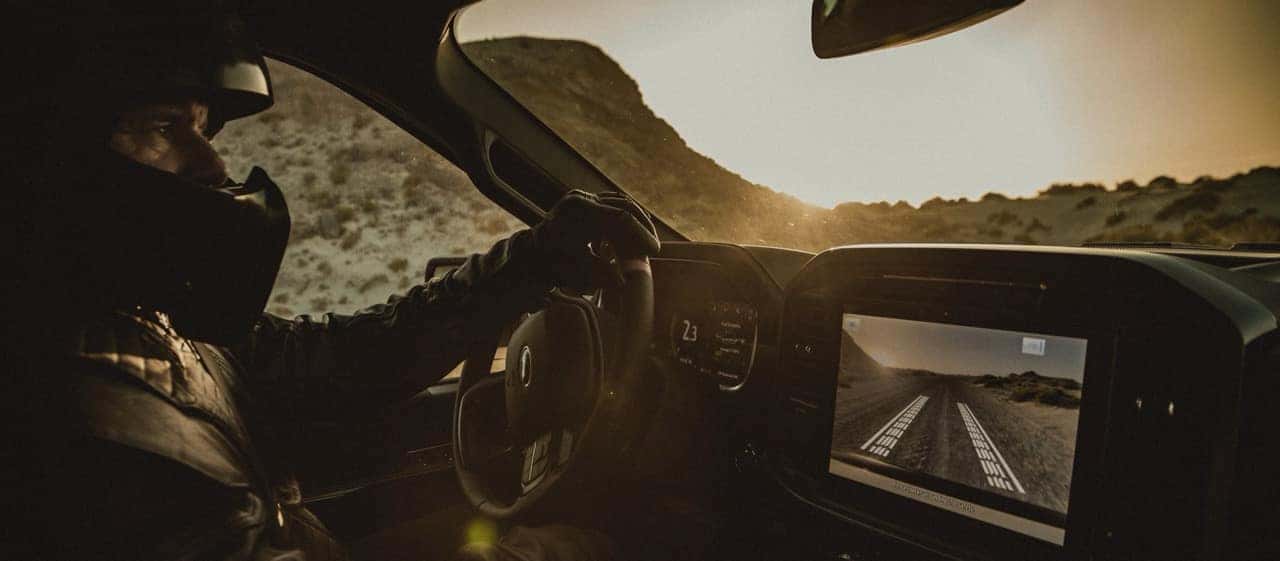 Man in a racing suit and helmet driving a 2025 Ford Raptor R through the desert