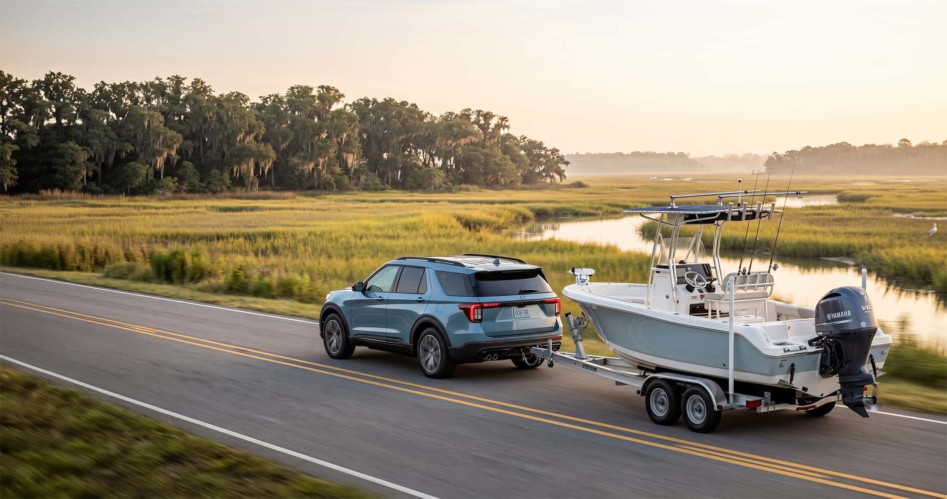 2026 Ford Explorer towing a center console fishing boat along a coastal Lowcountry road at sunrise with marsh and Spanish moss in the background