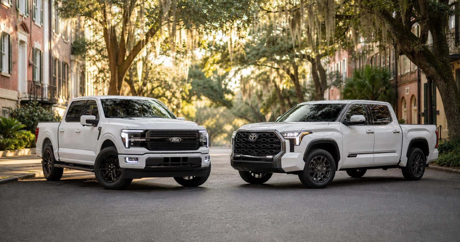 White Ford F‑150 and white Toyota Tundra parked on tree lined street under Spanish moss at sunrise showcasing front grille designs and trim level styling.