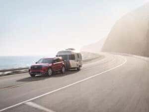red 2025 Ford Explorer towing camper on mountain road