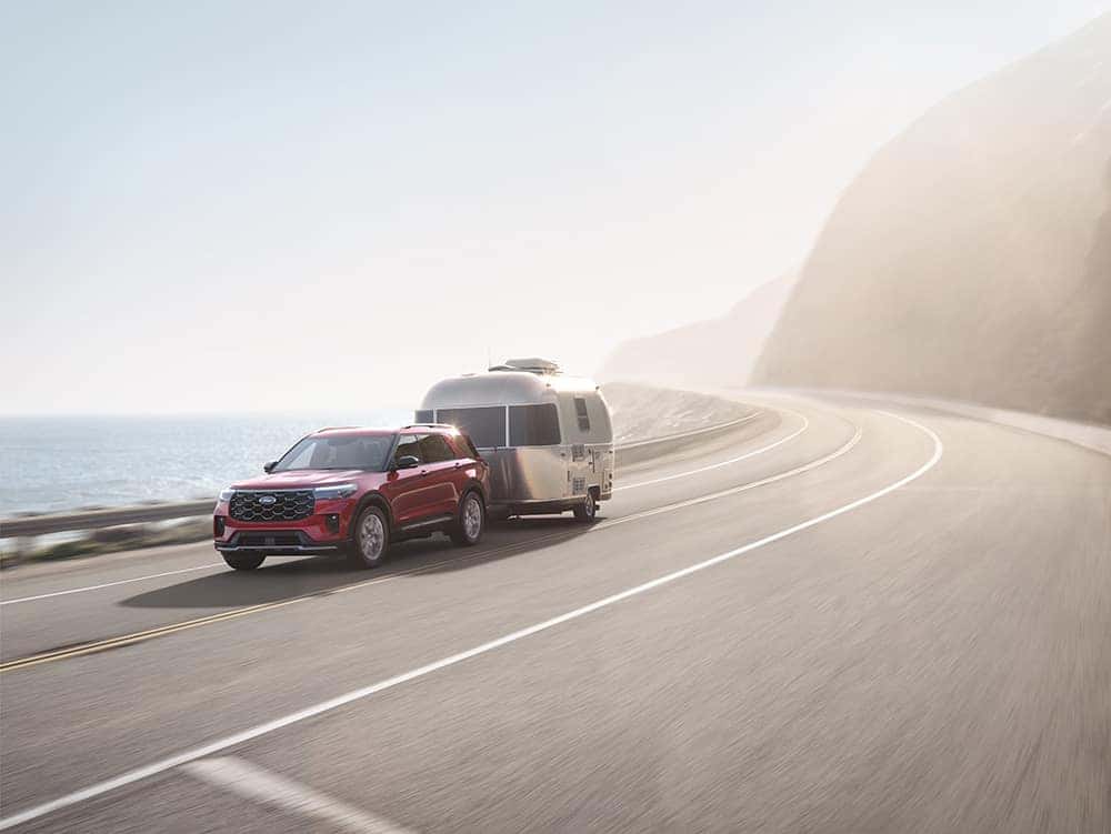 red 2025 Ford Explorer towing camper on mountain road