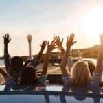 People holding hands out of convertible on road trip