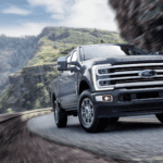 A lineup of Ford Super Duty trucks parked on display at a dealership, showcasing various trim levels including XL, XLT, LARIAT, King Ranch, and Platinum.