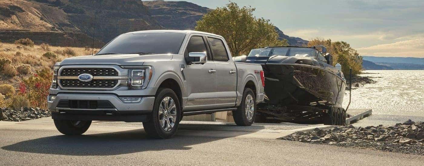 A silver 2023 Ford F-150 FX4 is shown towing a boat near a lake.
