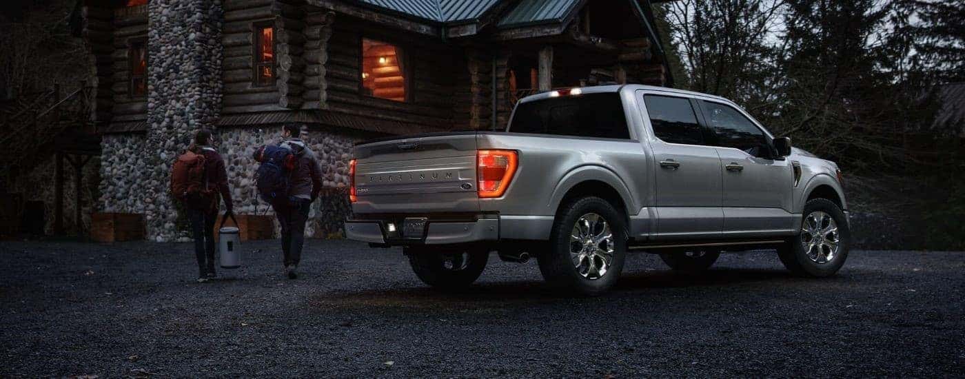 A silver 2023 Ford F-150 Platinum is shown from the rear parked next to a cabin at night.