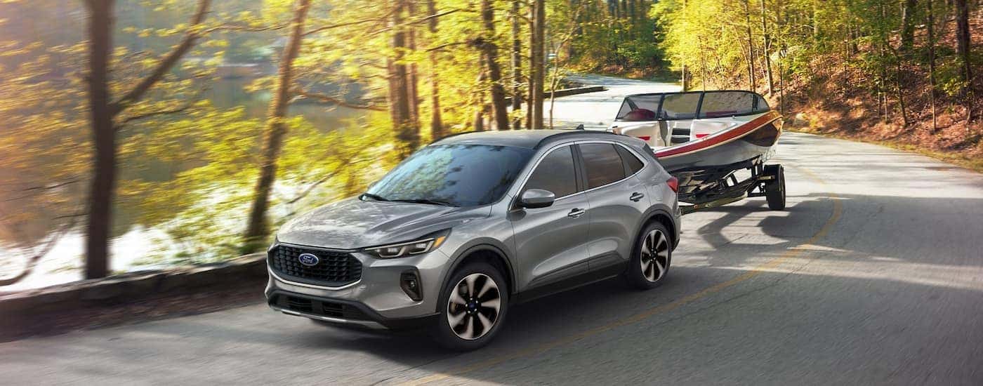 A silver 2024 Ford Escape is shown towing a boat next to a lake.