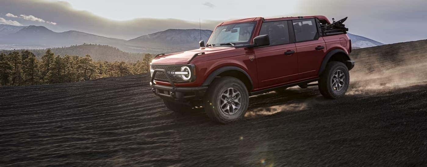 A red 2024 Ford Bronco is shown from the side driving on a dirt area.