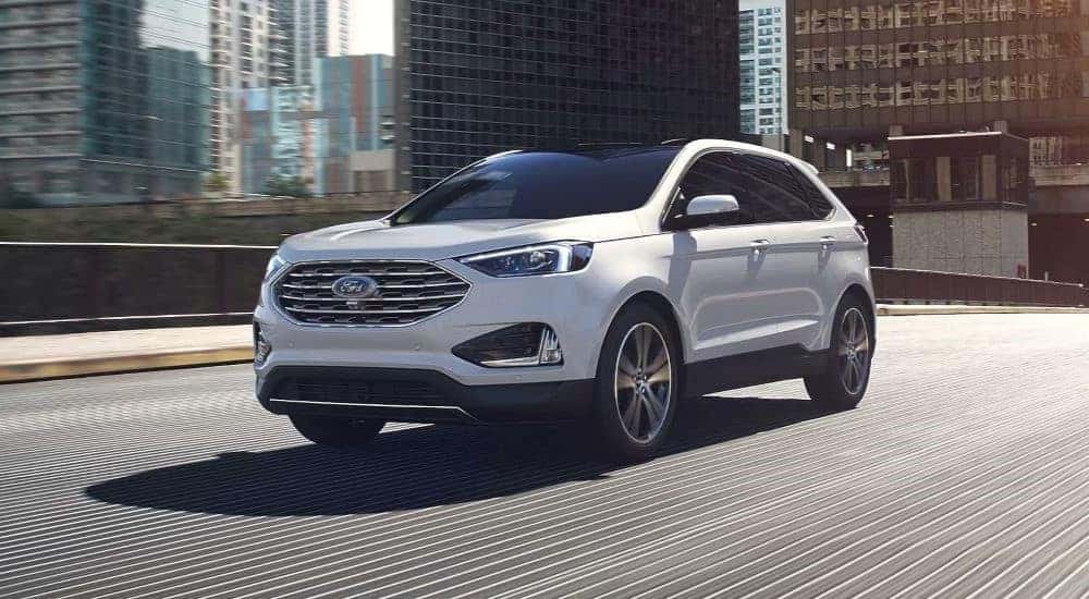 A white 2024 Ford Edge is shown driving in a city.