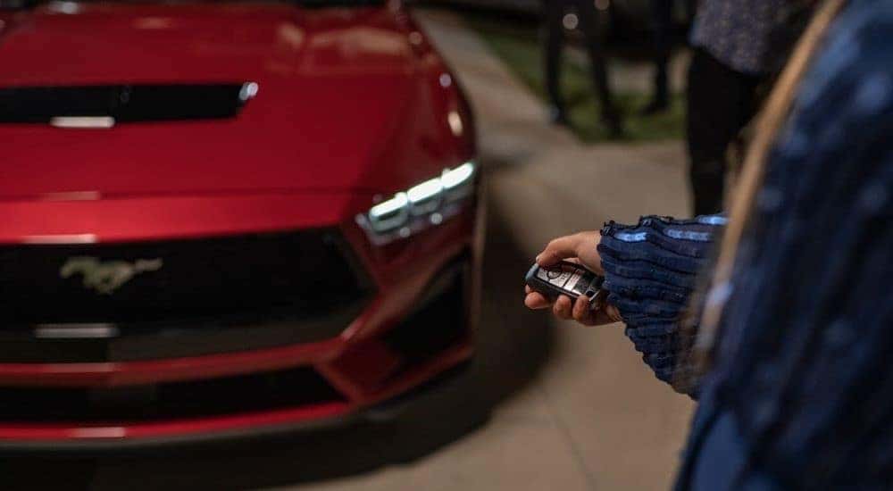 A person is shown pointing a key fob at the hood of a red 2024 Ford Mustang.