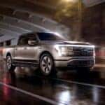 A silver 2024 Ford F-150 Lightning is shown driving through a rainy tunnel.