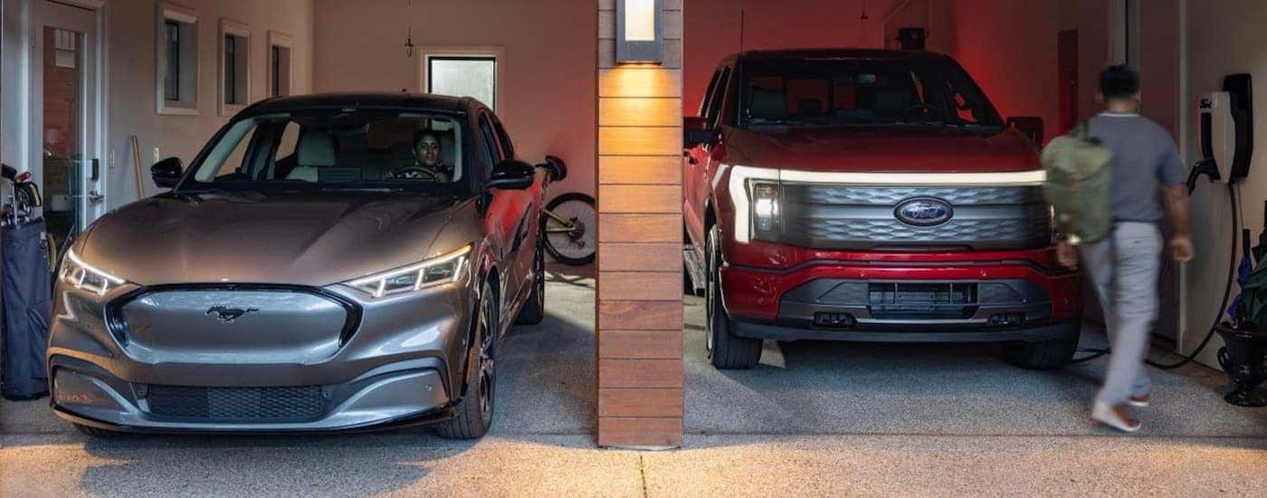 A grey 2024 Ford Mustang Mach-E and a red 2023 Ford Lightning are parked in a garage.