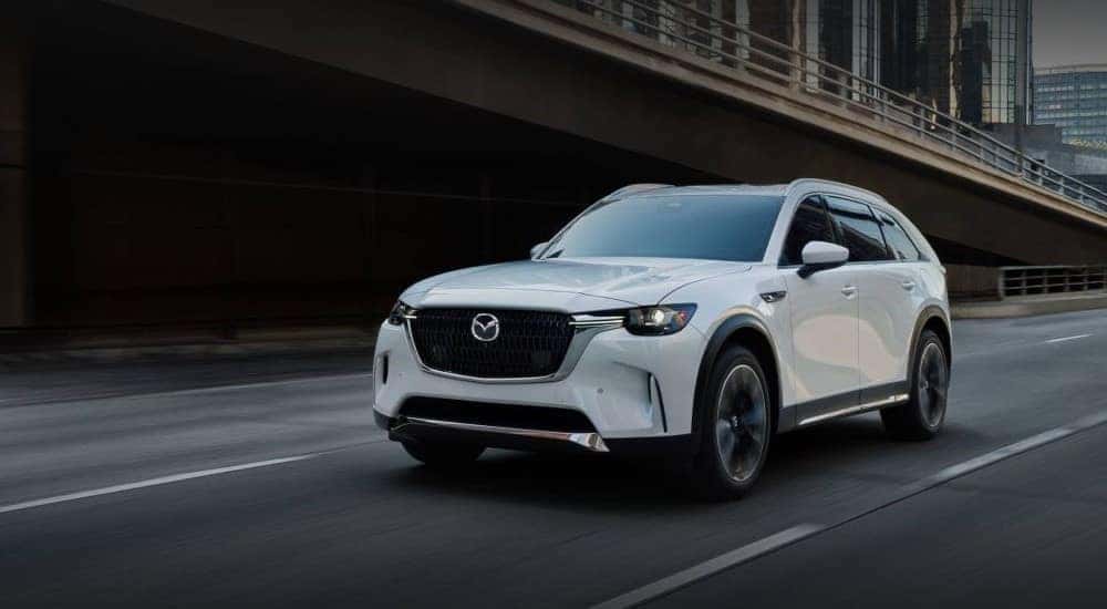A white 2024 Mazda CX-90 driving in a city.