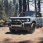A light blue 2025 Ford Bronco Sport Outer Banks driving off-road through the woods.