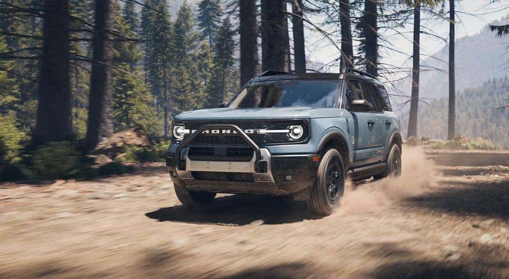 A light blue 2025 Ford Bronco Sport Outer Banks driving off-road through the woods.