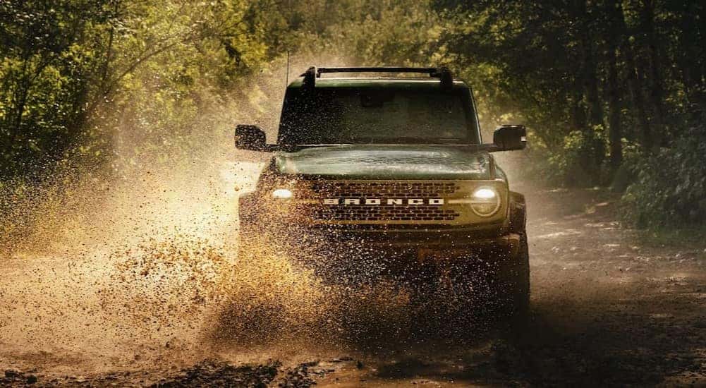 A green 2025 Ford Bronco splashing through mud.