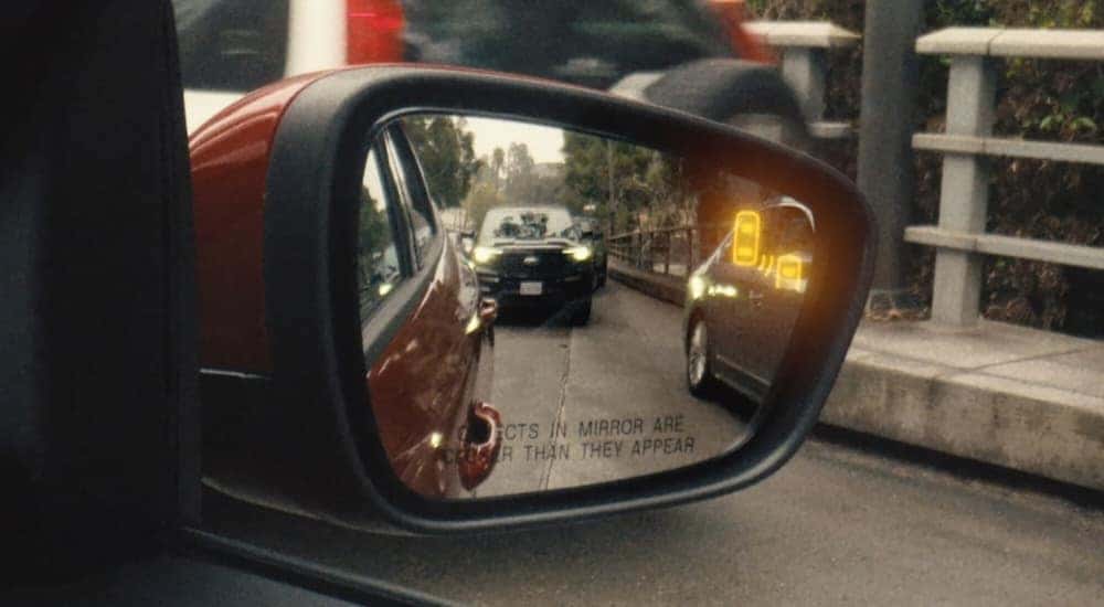 Illuminated blind spot monitoring icon on the mirror of a red 2025 Ford Escape.