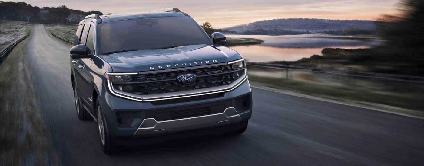 A blue 2025 Ford Expedition Platinum driving past a lake.