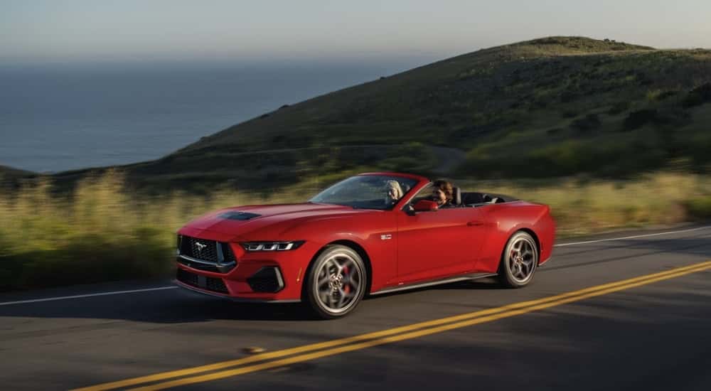 A red 2025 Ford Mustang GT is driving on a coastal road.
