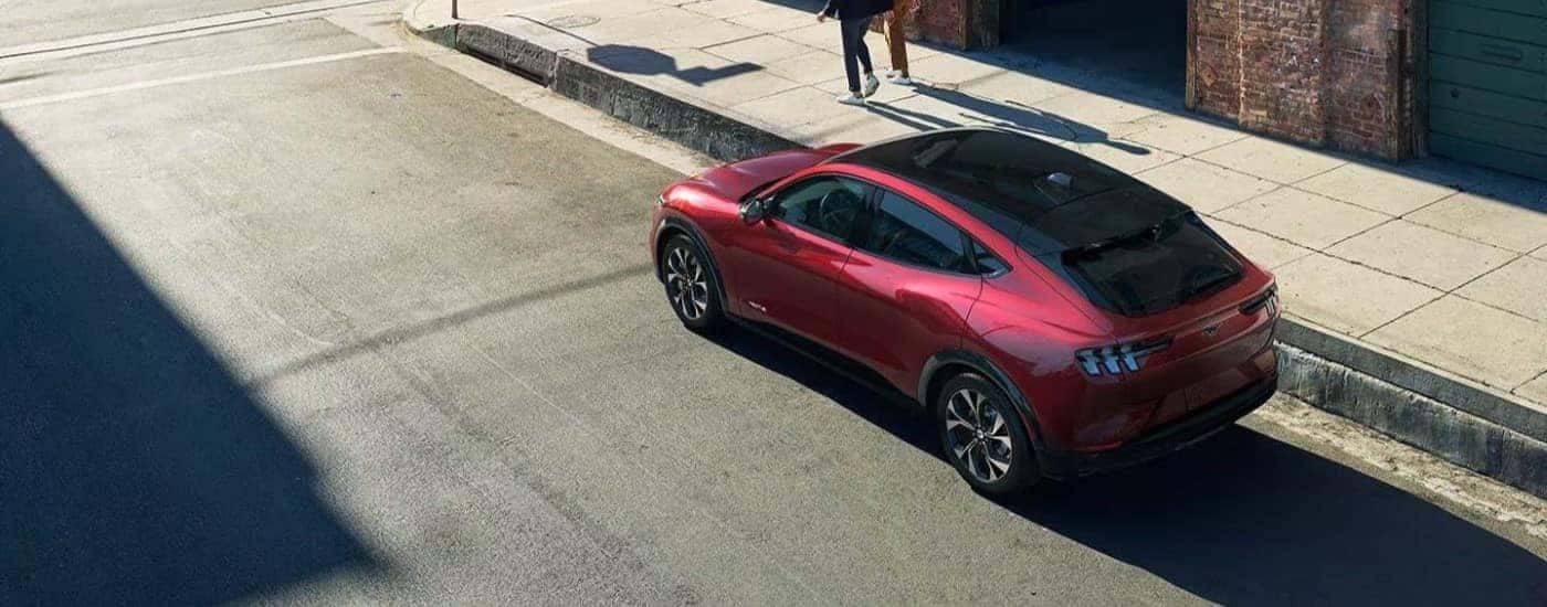 A red 2023 Ford Mustang Mach-E electric vehicle for sale is parked on the side of a city street.