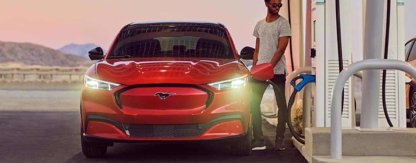A person is shown charging a red 2024 Ford Mustang Mach-E near a Ford dealer near Kennesaw.