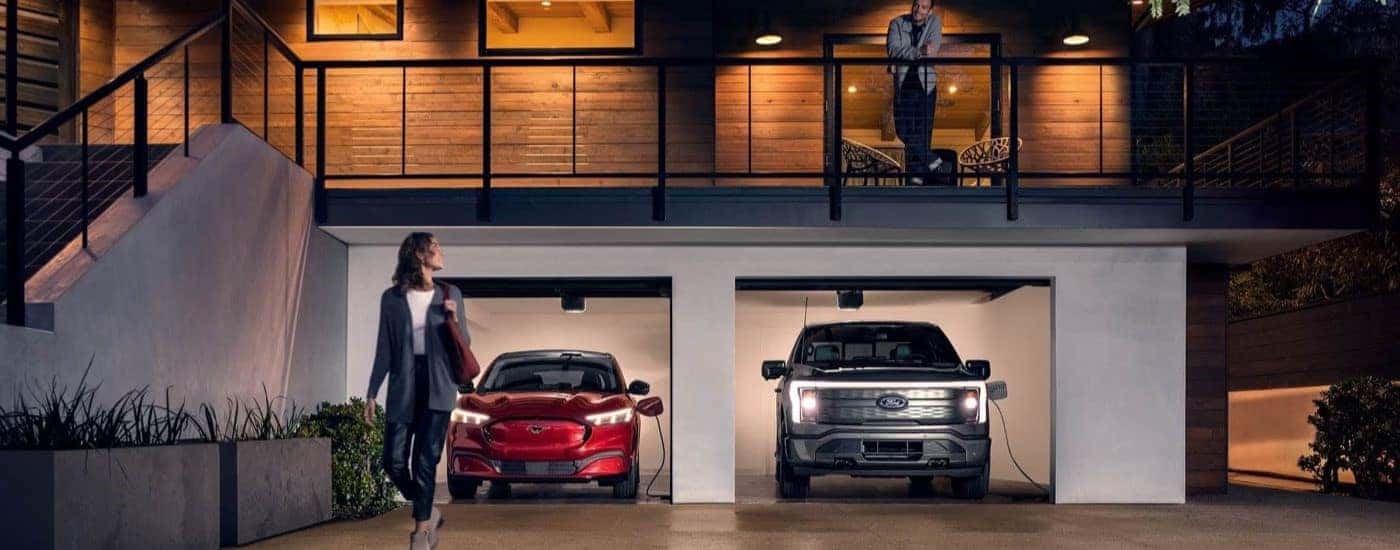 A red 2023 Ford Mustang Mach-E and a black F-150 Lightning are shown charging in a garage.
