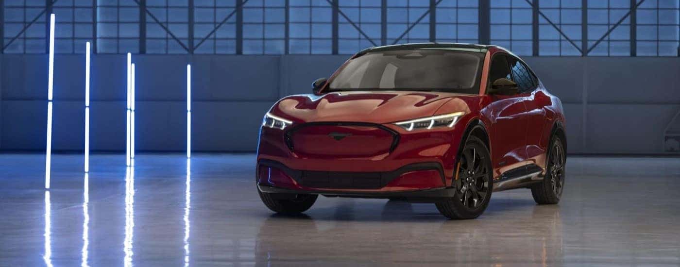 A red 2023 Ford Mustang Mach-E for sale is shown parked in a warehouse.