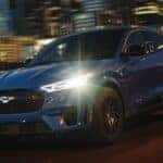 A blue 2025 Ford Mustang Mach-E driving down a highway at night