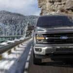 Dark grey 2025 Ford F-150 STX driving up mountain road.