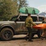 Two people carrying a kayak next to a dark green 2026 Ford Bronco.
