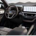 The modern interior of a 2026 Ford Explorer features a black dashboard with red contrast stitching, a multi-function steering wheel, and a large horizontal touchscreen infotainment display.