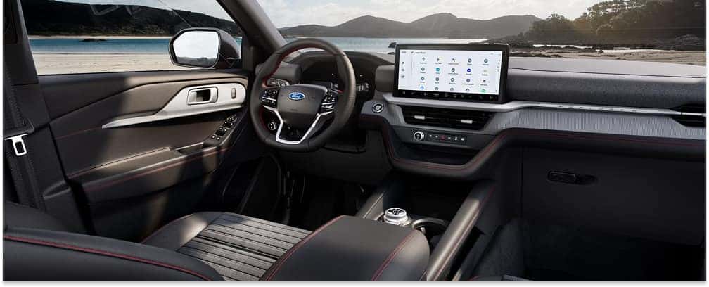 The modern interior of a 2026 Ford Explorer features a black dashboard with red contrast stitching, a multi-function steering wheel, and a large horizontal touchscreen infotainment display.