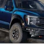 Blue 2026 Ford F-150 Raptor R driving off-road on a dirt trail, front three-quarter view.