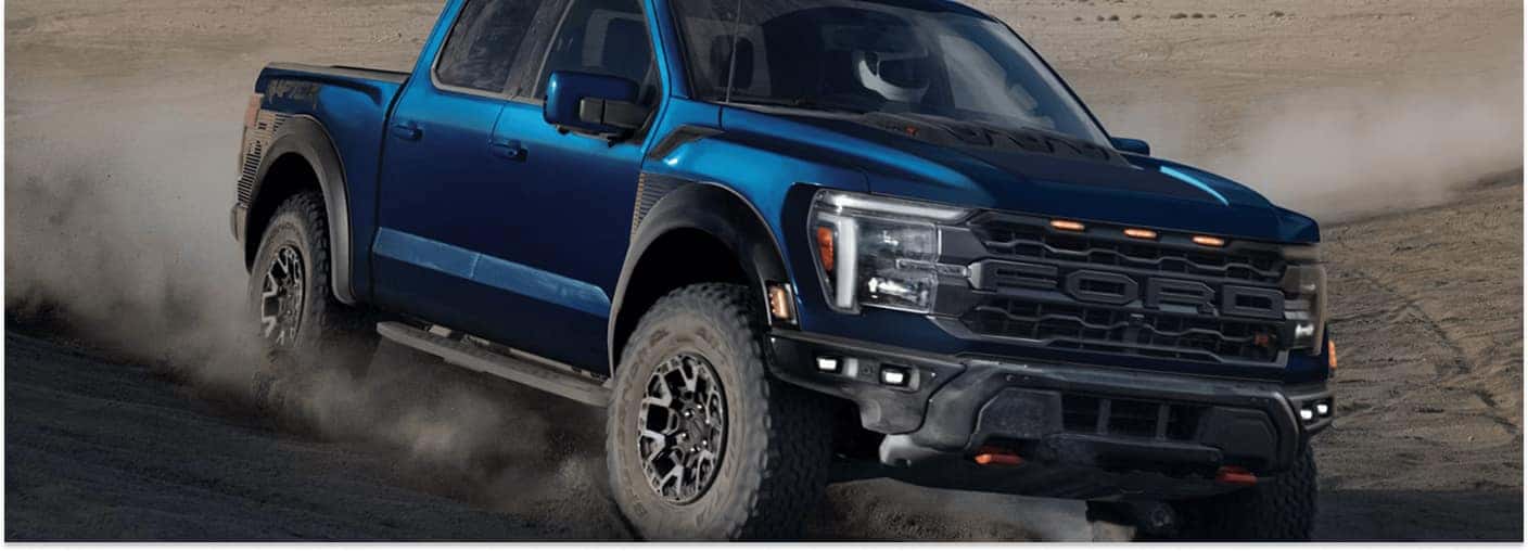 Blue 2026 Ford F-150 Raptor R driving off-road on a dirt trail, front three-quarter view.