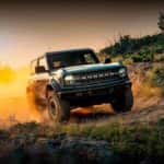 A blue 2022 Ford Bronco is shown kicking up dust off-road.