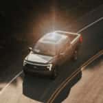 A grey 2023 Ford F-150 Lightning is shown driving to a Ford Lightning dealer.