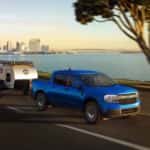 A blue 2023 Ford Maverick is shown towing a small trailer after leaving a Conyers Ford dealer.