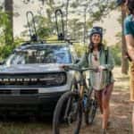Two people with bicycles are shown in front of a white 2023 Ford Bronco after leaving a Ford dealer.