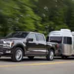 A grey 2024 Ford F-150 Platinum is shown towing a silver trailer after leaving a Ford dealer near Forest Park.
