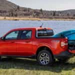 A red 2024 Ford Maverick FX4 with kayaks in the bed parked by water.