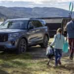 A family is walking near a blue 2025 Ford Explorer ST parked on a campsite near a lake.