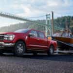 A red 2022 Ford F-150 Lariat pulling a boat out of a lake.