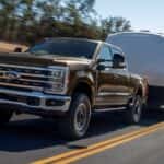 A brown 2025 Ford F-250 Tremor towing a camper on the highway.