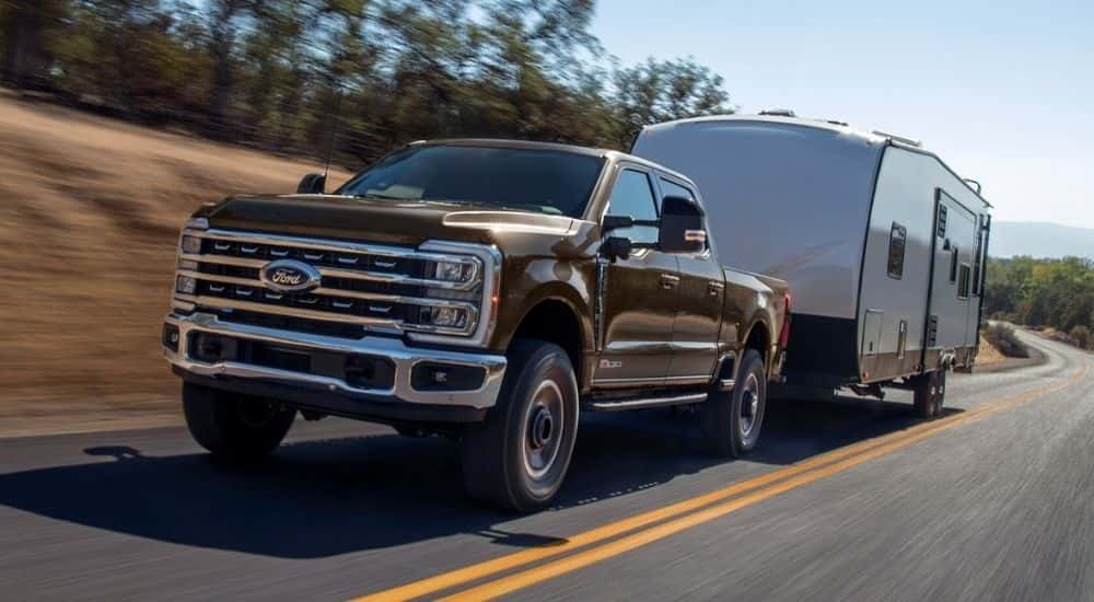 A brown 2025 Ford F-250 Tremor towing a camper on the highway.